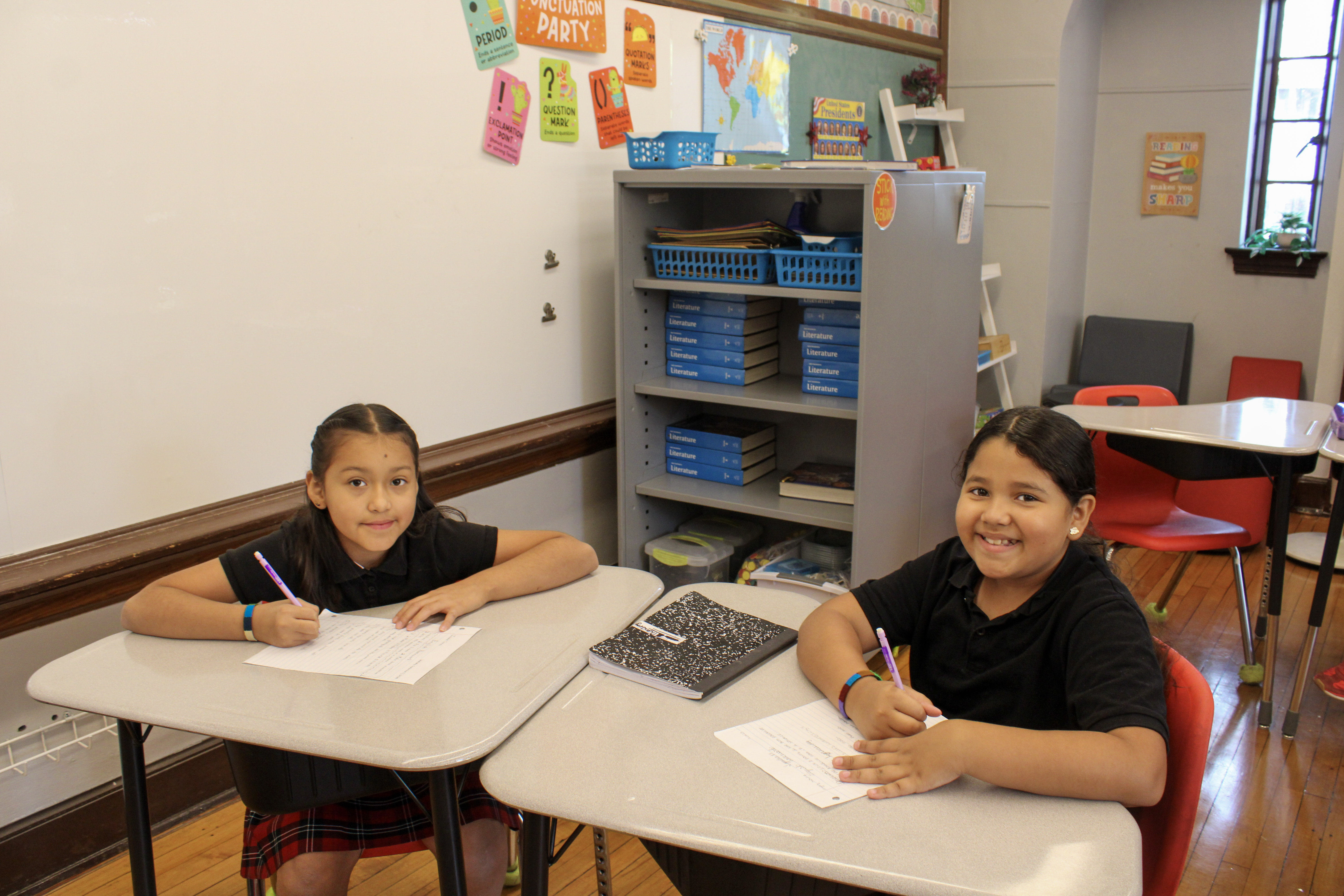 Two students at desks smiling.