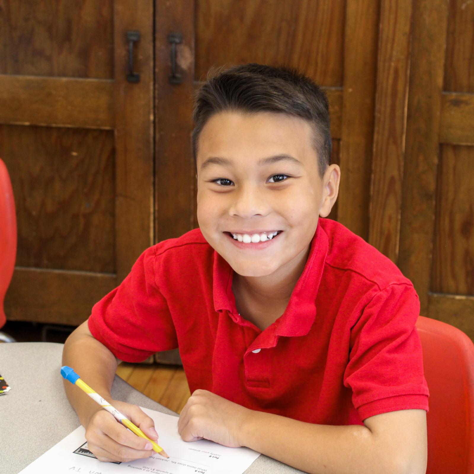 Young student smiling at camera with pencil and paper on desk